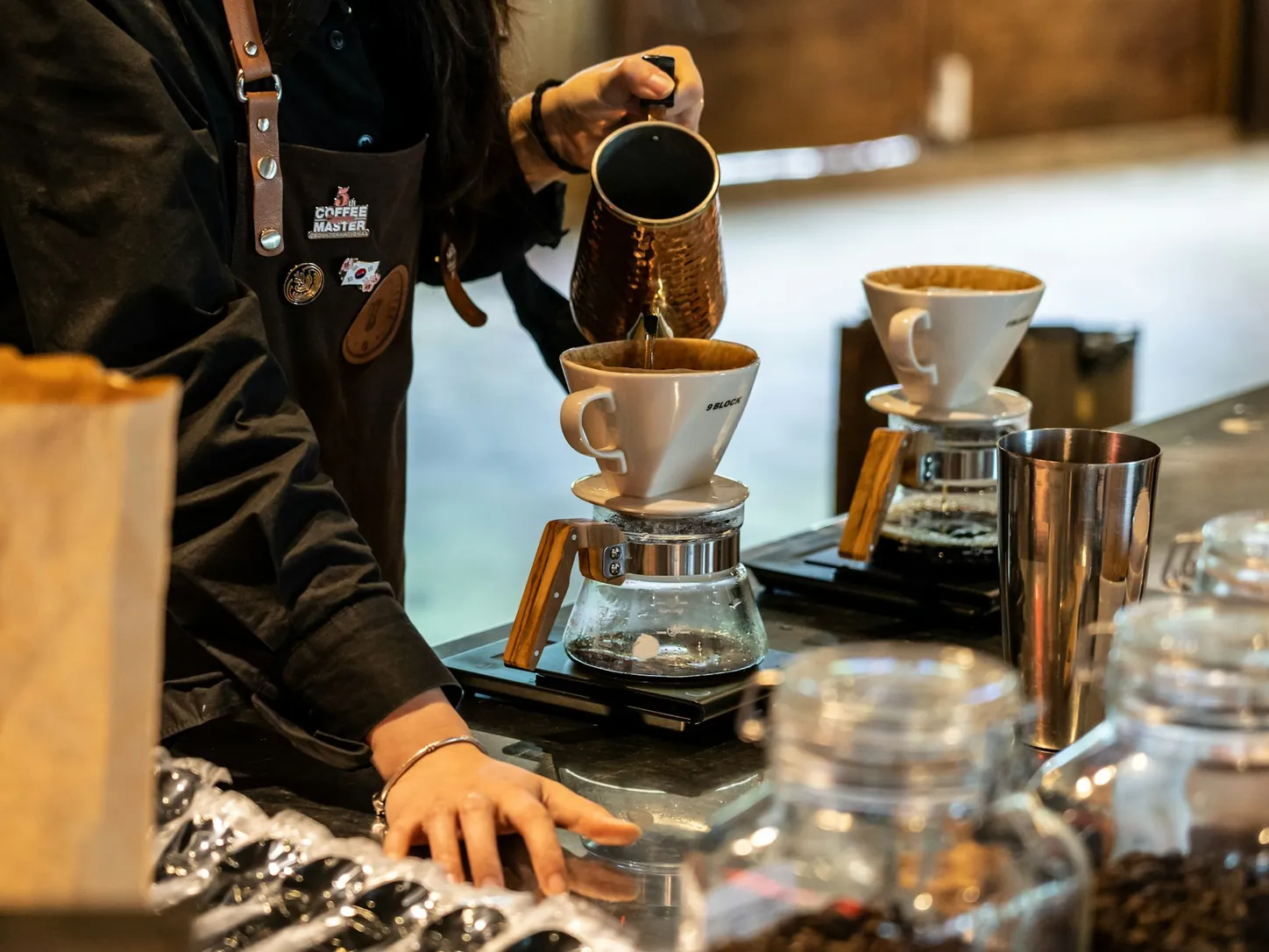 Barista toarnă apă fierbinte din ibric peste filtrele de cafea, la bar