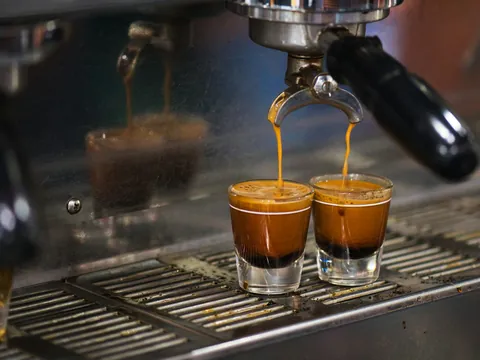 Două espresso curg din portafiltru în pahare mici de sticlă