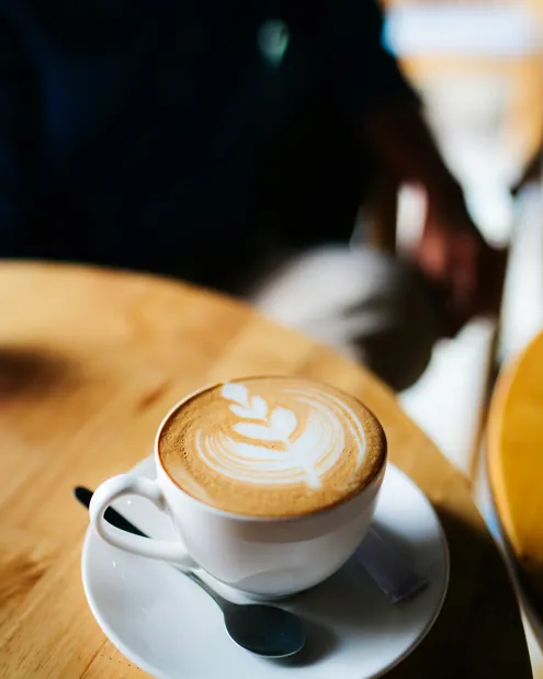 Cafea cu lapte cu frunză desenată în spumă, pe o masă de lemn